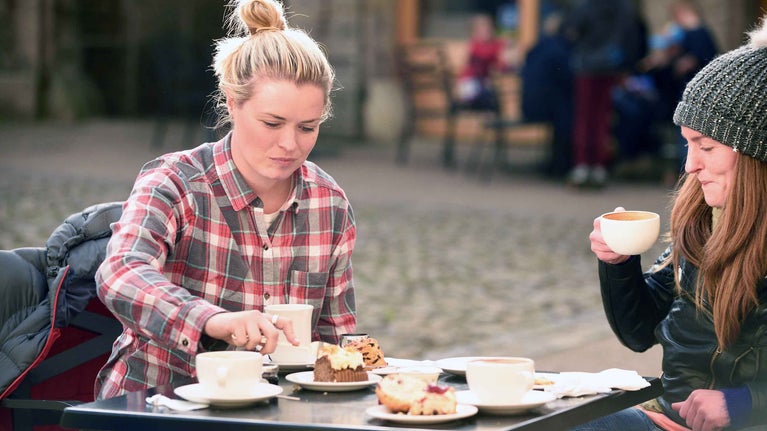 Two visitors sat with hot drinks and cakes on a table at Gibside